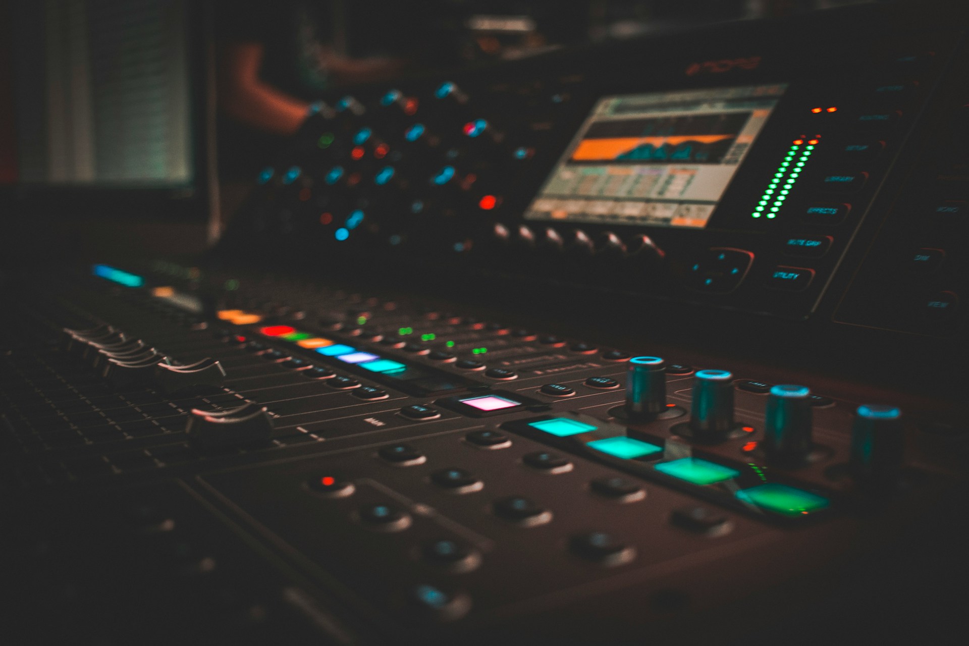 Close-up of a digital mixing console, faders and illuminated buttons in a darkened studio.